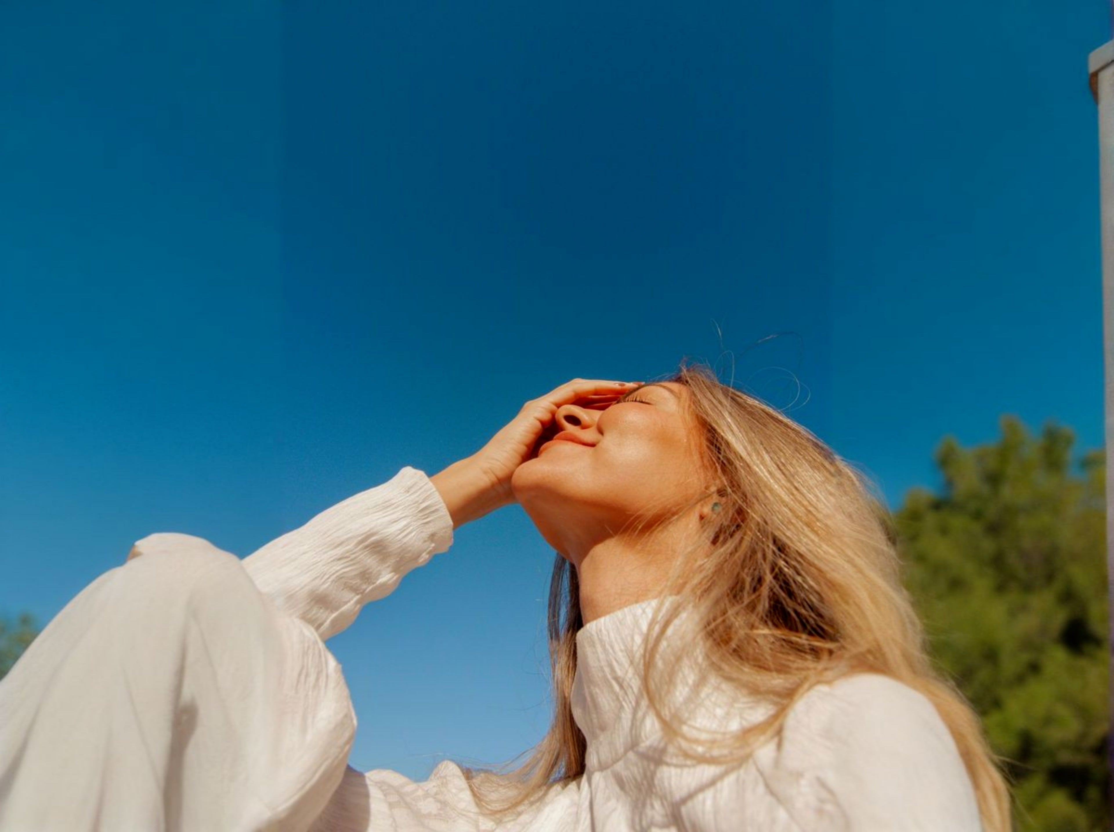Woman in a white outfit against a clear blue sky with greenery.